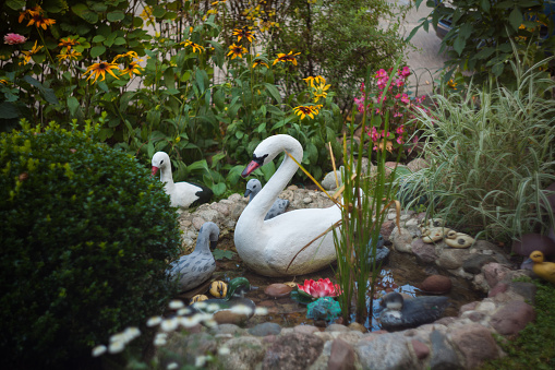 Decorative plastic flowers, swans and ducks in the artificial garden pond.