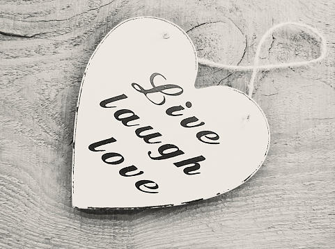 Decorative white wooden heart with the slogan live laugh love on grey wooden background.Live,Laugh,Love.Selective soft focus.Vintage filtered.