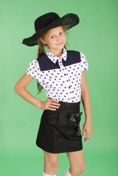 Young fashionable woman with black bob haircut, white shirt, black waistcoat and chequered skirt, leaning against a tree in a park, posing with her hands behind her head