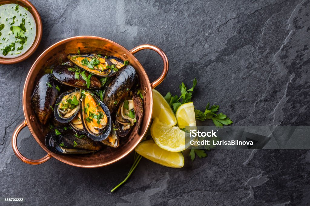 Mussels in copper bowl, lemon, herbs sauce and white wine. Shellfish Mussels in copper bowl with lemon and herbs. Shellfish seafood. Top view French Food Stock Photo