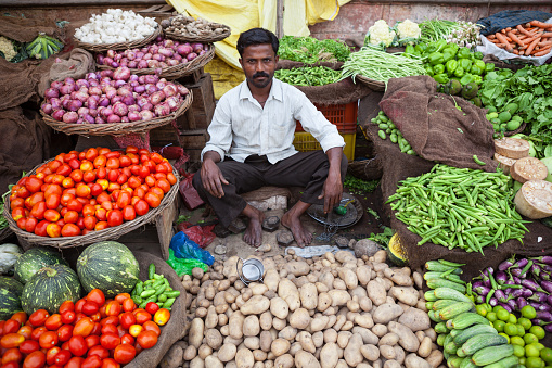 Varanasi, India - April 6, 2010: Indian greengrocer sitting in his store and waiting for customers.Large amount of vegetables and fruits such as tomato,potato,lemon,onion,beans etc are seen around him.