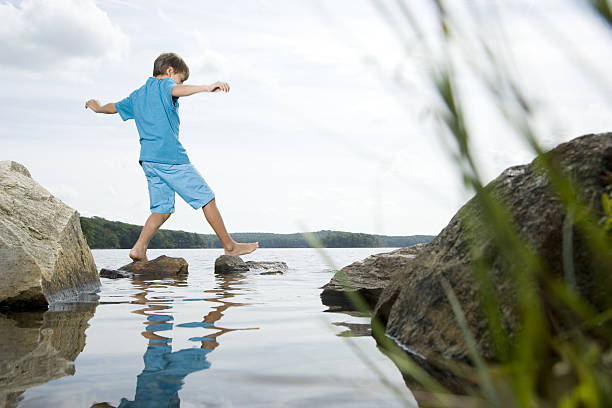 Boy walking barefoot across stones in lake