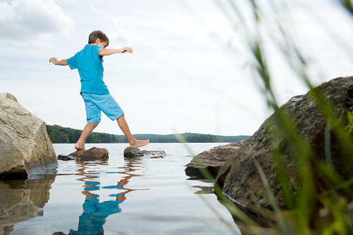 Boy walking barefoot across stones in lake