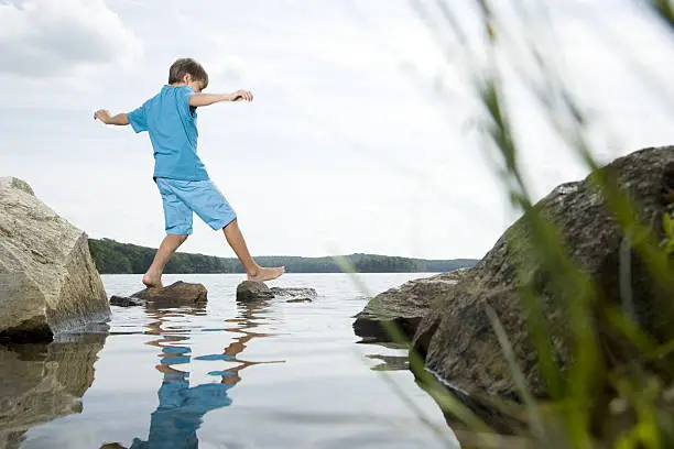 Photo of Boy walking barefoot across stones in lake