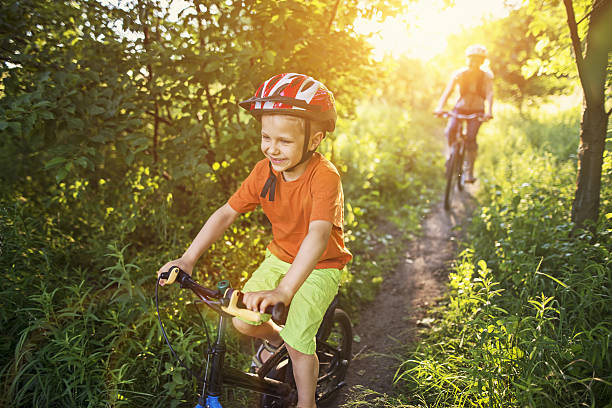Little boy with mother riding bicycles in forest or park on sunny summer day. 
