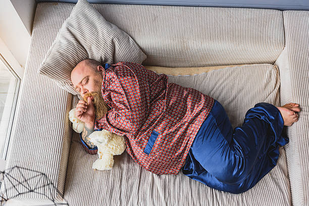 Fat guy sleeping on sofa Sleeping as bear. Calm thick man is napping on couch with soft toy. He is lying and sucking his finger man with teddy bear stock pictures, royalty-free photos & images