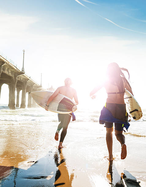 surfeurs de jogging sur la plage en entrant sur l'eau - spraying beaches summer sunlight photos et images de collection