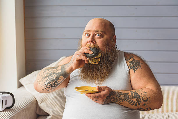 fat-man-eating-unhealthy-burger-at-home.jpg?s=612x612&w=0&k=20&c=urBjb--0NtVtgpuAMubdHjJS9UoULv03bcumj6LszDY=