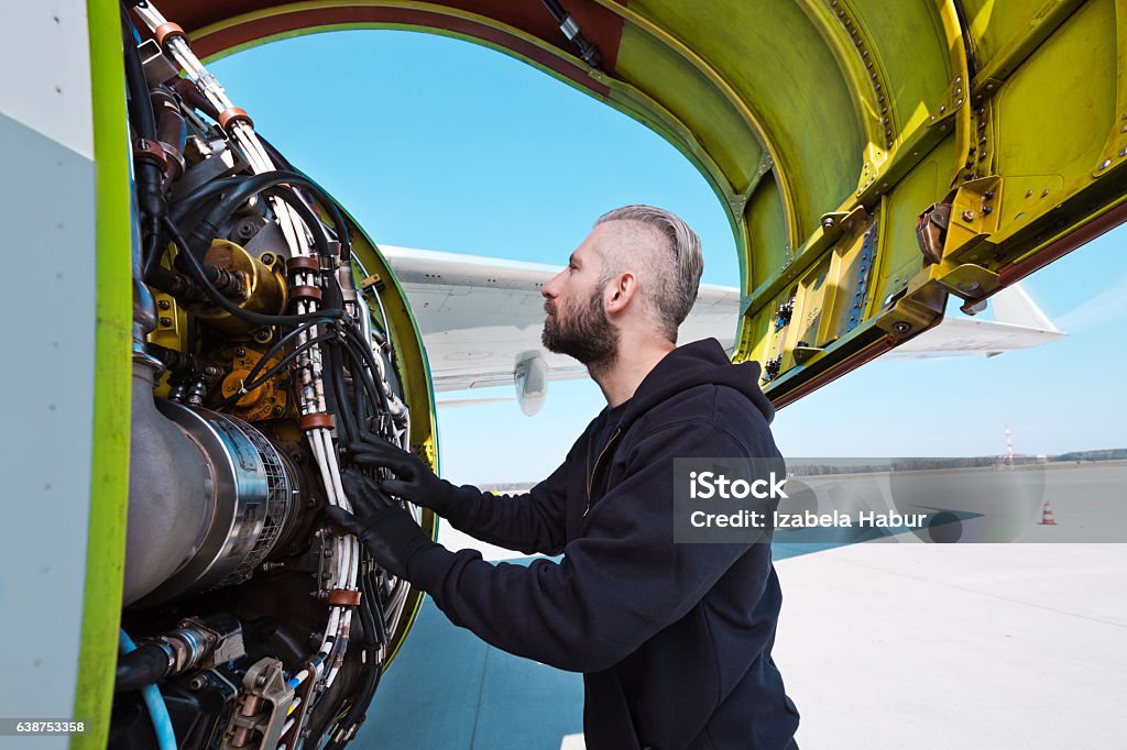 Aircraft mechnic examining aircraft engine Aircraft mechanic standing outdoor in front of airplane engine. Adult Stock Photo