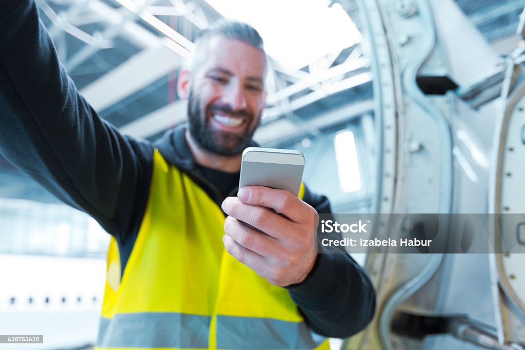 Aircraft engineer using a smart phone in a hangar Aircraft engineer using a smart phone in a hangar. Close up of hand. Airplane Mechanic Stock Photo