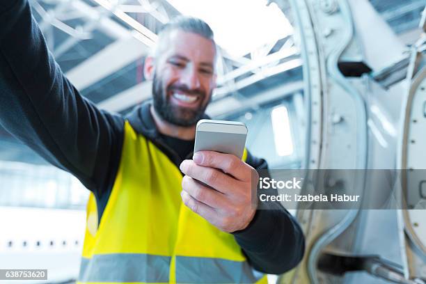 Aircraft Engineer Using A Smart Phone In A Hangar Stock Photo - Download Image Now - Airplane Mechanic, Smart Phone, Adult