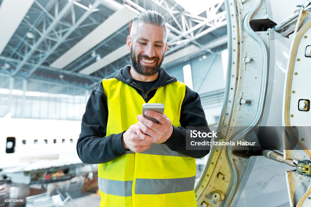 Aircraft engineer using a smart phone in a hangar Aircraft engineer using a smart phone in a hangar.  Airplane Stock Photo