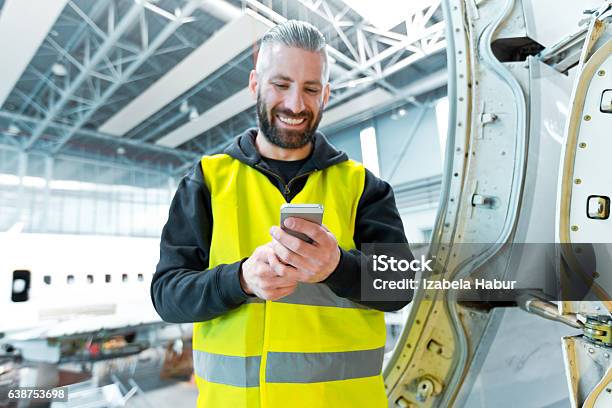 Aircraft Engineer Using A Smart Phone In A Hangar Stock Photo - Download Image Now - Airplane, Repairing, Telephone