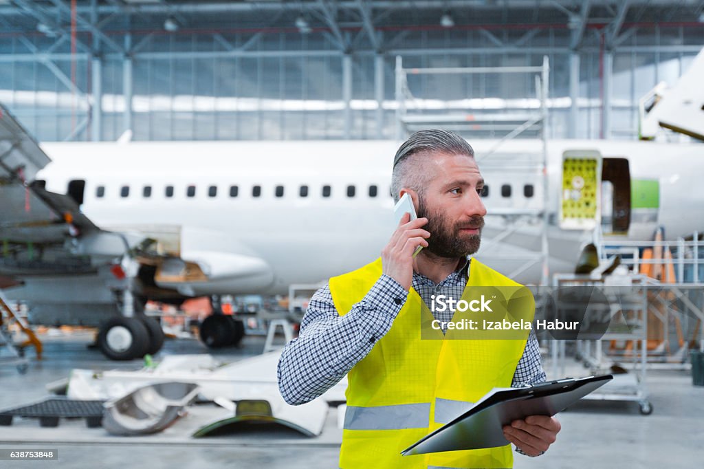 Aircraft engineer talking on mobile phone in a hangar Aircraft engineer talking on mobile phone in a hangar, holding a clipboard in hand. Manager Stock Photo