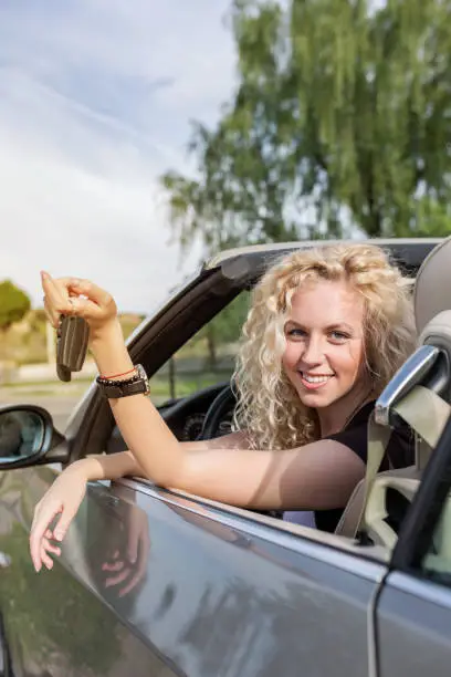 Young woman turning towards the camera while sitting in her new convertible car and showing car keys.