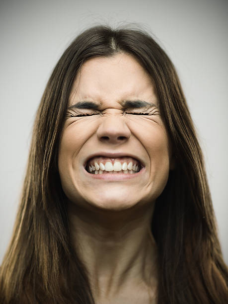 Angry young woman clenching teeth Close-up of angry young woman clenching teeth. Aggressive female is with eyes closed. She is against gray background. Vertical studio photography from a DSLR camera. Sharp focus on eyes. bad teeth stock pictures, royalty-free photos & images
