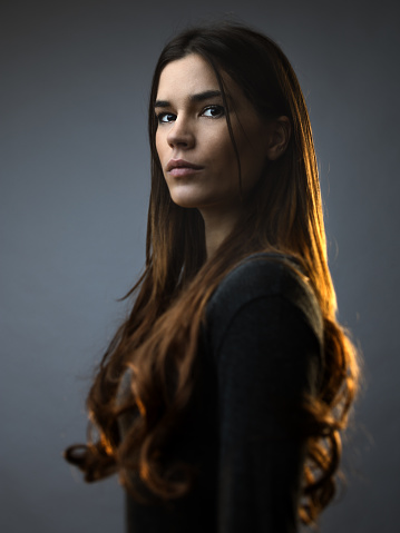 Beautiful woman posing against against grey background. Beautiful female with long brown hair is standing. She is wearing casual clothes. Vertical studio photography from a DSLR camera. Sharp focus on eyes.