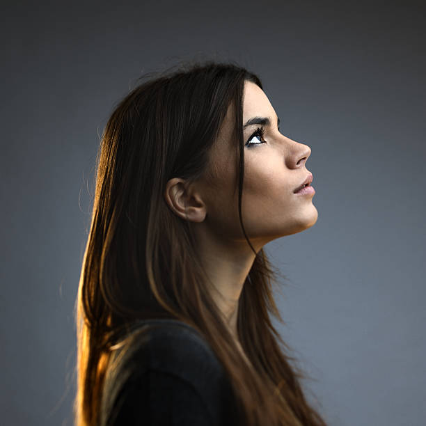 Beautiful woman posing against dark background Beautiful woman posing against against grey background. Beautiful female with long brown hair is standing. She is wearing casual clothes. Square studio photography from a DSLR camera. Sharp focus on eyes. profile view stock pictures, royalty-free photos & images