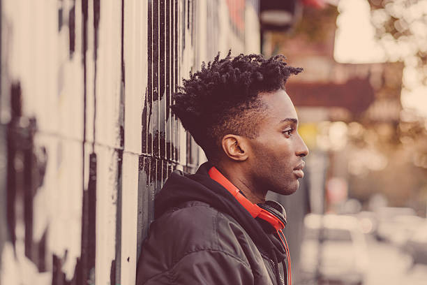 Side view of afro american guy wearing black bomber jacket, on the street in the city.