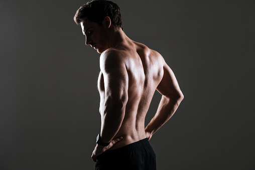 Back view image of handsome sportsman standing in gym over grey background.