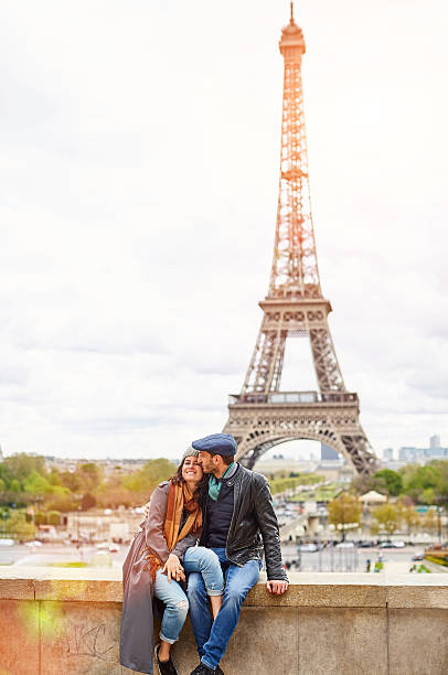 They could be anywhere as long as they're together Shot of a happy young couple sitting together in front of the Eiffel Tower paris france eiffel tower love kissing stock pictures, royalty-free photos & images