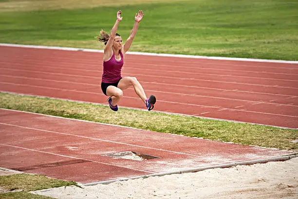Shot of a young woman in mid air doing a long jump on a sports field