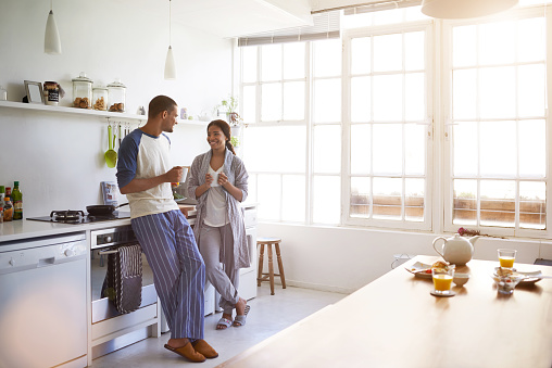 Shot of a young couple talking together and drinking coffee in their kitchen in the morning