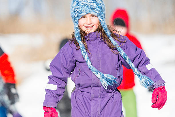 A multi-ethnic group of elementary age children are ice skating on a frozen lake on a sunny winter day. One girl is smiling and looking at the camera.