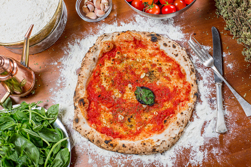 Traditional italian pizza with tomato sauce, garlic, basil and oregano on a wooden table with the ingredients