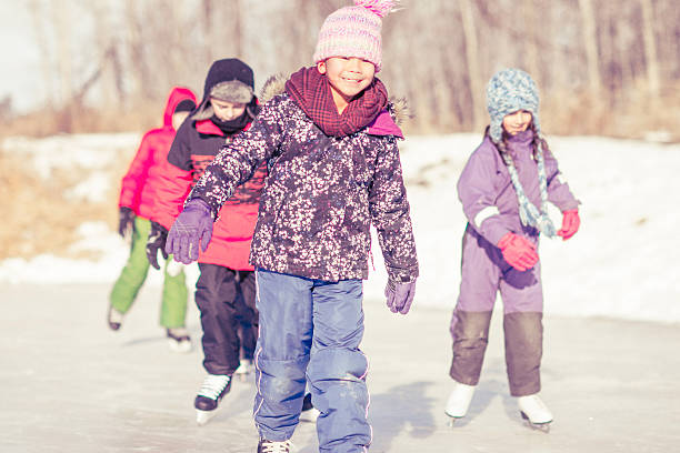 A group of elementary age children are ice skating on a frozen lake on a sunny winter day.