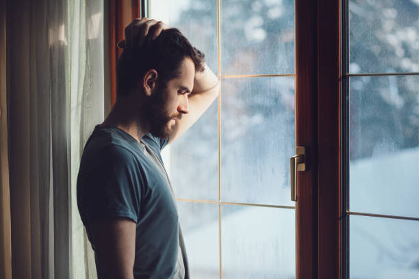 Young sad mad sitting by the window Young sad mad sitting by the window in regret depression sadness stock pictures, royalty-free photos & images
