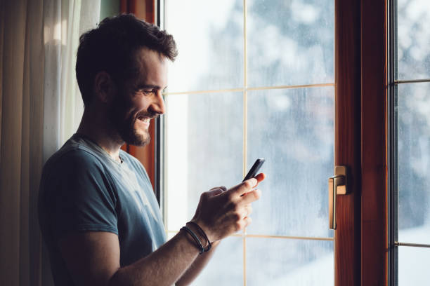 istock Young man standing by the window using a smartphone 638784684