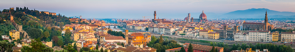 Blue ridges of the Apennine hills framing the iconic terracotta rotunda and gothic marble facade of Brunelleschi's magnificent Renaissance masterpiece, the Basilica di Santa Maria del Fiore or Duomo as it towers above the crowded rooftops of Florence, Italy.