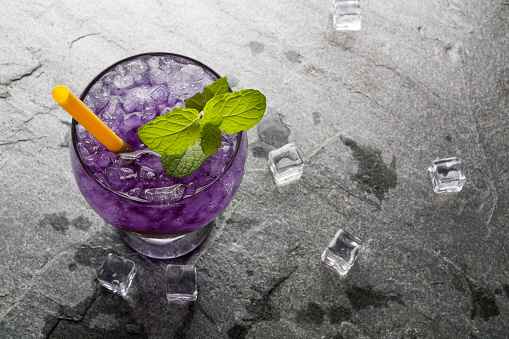 Purple soda lime drink with lime on stone.