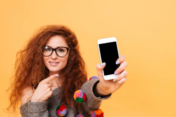 istock Woman holding mobile phone and pointing it isolated on orange 638792552