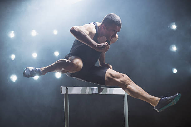 athlete jumping over hurdle - hurdling imagens e fotografias de stock