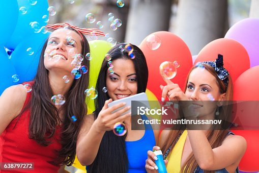 istock Cheerful friends holding colored balloons and making soap bubbles 638797272