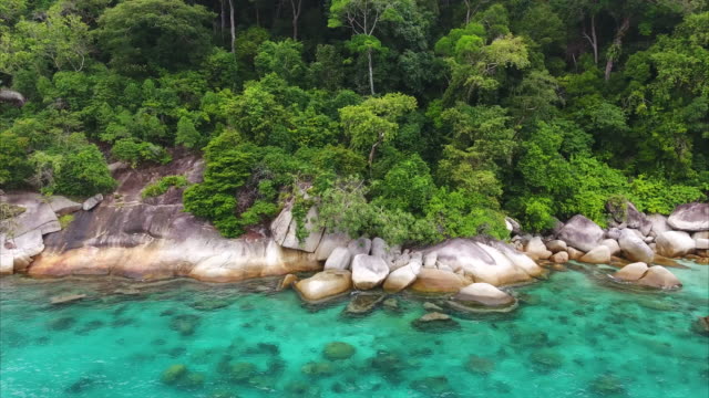 Aerial slow pan of rocky coastline in beautiful tropical clear water