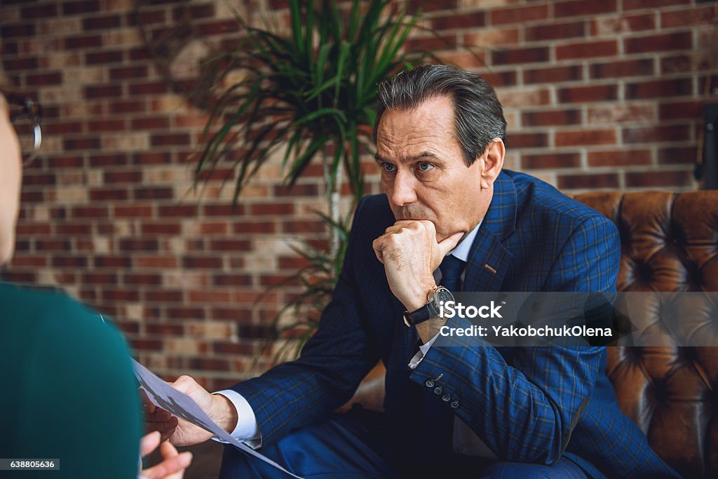 Attentive mature man in office of psychologist Middle aged frowning businessman is sitting on couch. He hardly thinking about image on paper Discussion Stock Photo