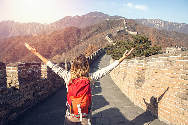 Young woman embracing nature-Great Wall of China Young woman on top of the Great Wall of China arms outstretched for freedom and positive emotions. Contemplating the beautiful landscape from high up.  great wall of china stock pictures, royalty-free photos & images