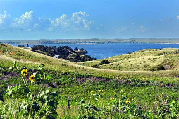 Rolling Nebraska grassland slopes down to blue, Lake McConaughy.  Tiny white sailboats dot small bay.
