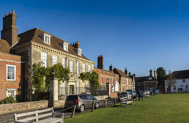Salisbury, UK - January 18, 2017: A row of multiple historic buildings on Cathedral Square in Salisbury. The largest buildnig is Mompesson House. Cars parked on the road. A small group of people sit on park benches. 