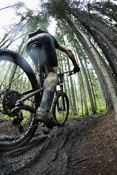 A man competes in a mountain bike race on a wet and muddy course in the rain. 