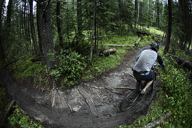 A man competes in a mountain bike race on a wet and muddy course in the rain.