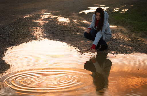 A darkhaired women reflected in puddle. Clouds on sunset reflecting in the water. bright colors.