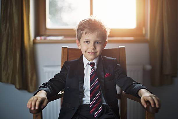 Portrait of a cute little business man or politician Portrait of a smiling cute blonde boy wearing a suit and a tie. The boy is aged 6 and is sitting in a chair and smiling at the camera. chairperson stock pictures, royalty-free photos & images