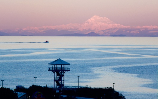 On a cold clear evening the spectacular view at sunset above the Tower of the City Pier in Port Angeles Washington across the Strait of Juan de Fuca to the snowcapped Mt. Baker in the Cascade mountains a distance of over 90 miles.