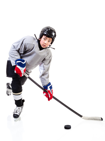 Junior ice hockey player with full equipment and uniform posing for a shot with a puck. Isolated on white background.