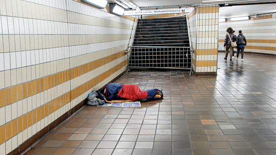 London, UK: October 01, 2013: A homeless man is sleeping on the floor in the Northumberland Avenue underground station. He is facing the camera and three people have walked past. 