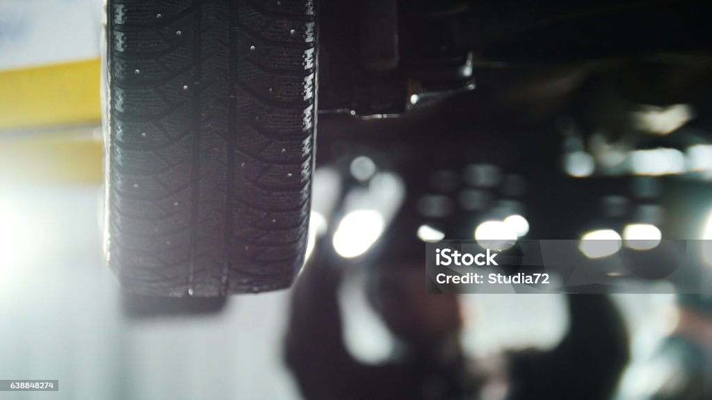 Car service - mechanic unscrewing device while working under lifted Car service - mechanic unscrewing automobile device while working under a lifted car, wheel, close up Adjusting Stock Photo